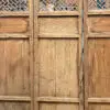 Three tall, weathered wooden doors with decorative lattice panels at the top and solid lower panels, standing closed in a row.