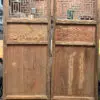 Two tall rustic wooden doors with carved lattice screens at the top and paneled solid bottoms, standing in a workshop setting.