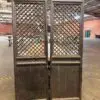 Two tall dark wooden doors with diamond lattice panels standing upright in a workshop/warehouse setting.