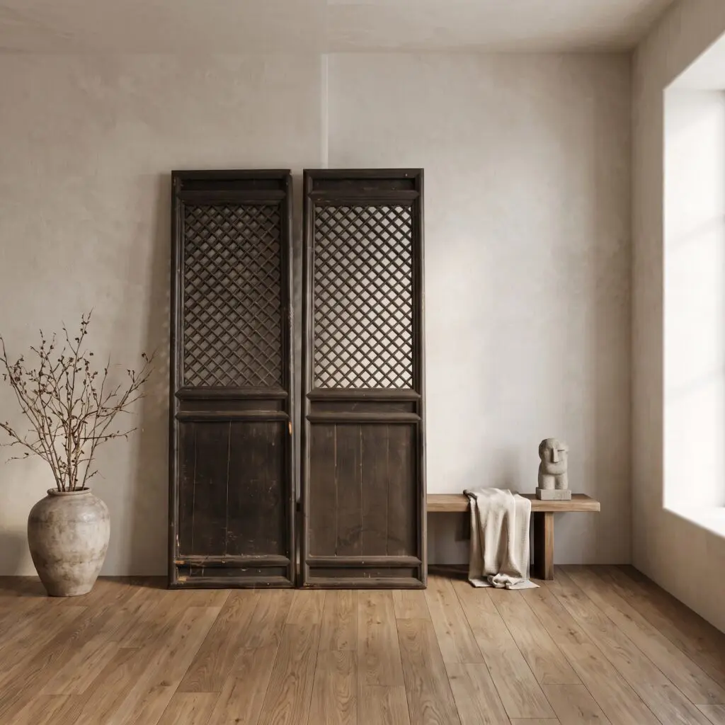 Two tall dark wooden cabinets with lattice fronts stand against a beige wall, flanked by a vase with dried branches on the left and a small sculpture on a wooden table on the right.