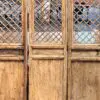 Three tall, weathered wooden doors with diamond lattice panels and bottom panels revealing a glimpse of the interior behind.