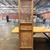 Tall antique wooden cabinet with a lattice front, standing on a table in an industrial warehouse.