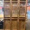 Three tall wooden lattice panels standing side by side in a warehouse, forming decorative room dividers.