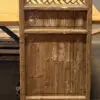 Rustic wooden cabinet with a woven lattice upper panel and weathered lower panels, standing on a concrete floor.