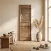 Rustic interior with a tall wooden cabinet featuring a woven lattice panel, pampas grass vase by a window, and warm beige walls.