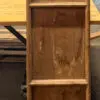 Tall rustic wooden cabinet with worn, paneled doors and a simple frame, standing on a concrete floor beside a wooden table.