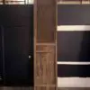 Tall weathered wooden cabinet with a lattice panel, standing against a dark wall with white stripes in an industrial space