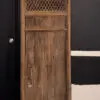 Weathered wooden door with diamond lattice panel at top, leaning against a black wall beside a modern black door.