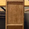 Weathered wooden cabinet with vertical panels and recessed door sections, standing on a workshop floor