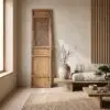Warm minimalist living room corner with a tall wooden cabinet, beige textured walls, and a lattice panel, plus a vase of bare branches and a checkered sofa.