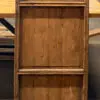 Tall antique wooden cabinet with two small upper drawers and paneled doors, weathered brown finish in a workshop setting.