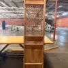 Tall wooden cabinet with a lattice central panel, standing on a table in a large, empty warehouse.