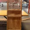 Tall wooden cabinet with a woven lattice screen on the upper door, placed on a wooden table in an industrial warehouse setting.