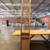Tall wooden lattice screen standing upright on a table in a large warehouse with brick walls and scattered furniture in the background.