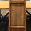 Tall, weathered wooden cabinet with beveled panels standing on a concrete workshop floor