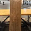 Wooden carved pillar with geometric lattice at top and a bas-relief panel in the middle, placed on a wooden platform in an industrial workshop.