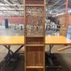 Tall wooden screen with a geometric lattice panel, standing on a table in a warehouse setting.