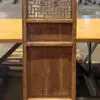 Tall wooden cabinet/room divider with a decorative geometric lattice panel at the top, standing on a table in a warehouse setting, with solid lower panels.