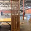 Tall wooden lattice panel or room divider standing upright in an industrial warehouse, with tables and pallets in the background.