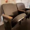 Row of vintage brown upholstered theater seats with wooden armrests in a worn, industrial space