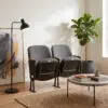 Indoor seating area with a black floor lamp, grey chairs, and a tall potted plant near a coffee table with books on a woven rug.