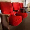 Red velvet theater seats with wooden armrests in an industrial, brick-walled room.