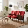 Living room with red upholstered chairs arranged in a row, a round wooden coffee table, and several green plants by a light wall with a framed abstract artwork.