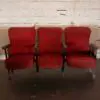 Three red cushioned theater chairs in a row against a rough white brick wall.