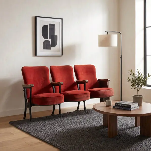Row of red upholstered chairs arranged along a wall with a black-framed abstract print, a tall floor lamp, and a potted plant in a modern lounge area.