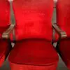 Red upholstered theater chair with wooden armrests, centered between other red seats.