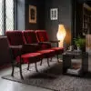 Row of red upholstered theater chairs along a dark wall with a tall glowing floor lamp and framed art above.
